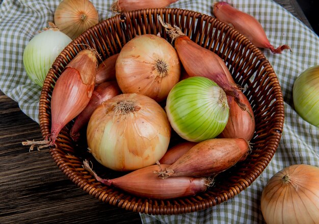 Vue latérale des oignons comme des échalotes sucrées et blanches dans le panier sur tissu à carreaux et fond en bois