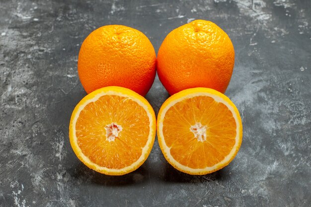 Vue latérale d'oranges fraîches biologiques naturelles entières et coupées alignées en deux rangées sur fond sombre