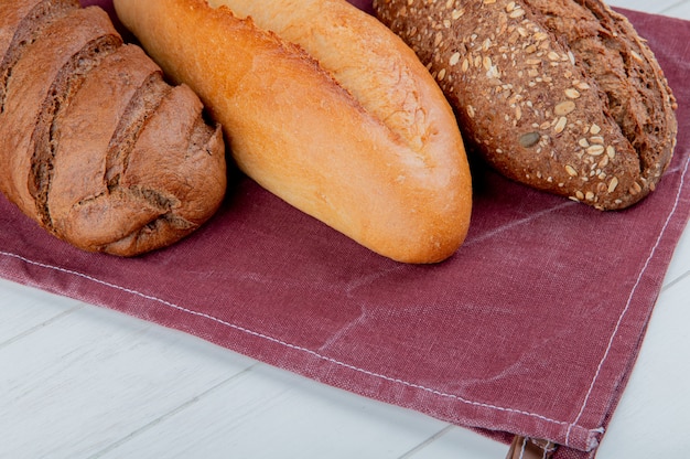 Vue latérale des pains comme baguette vietnamienne et noire et pain noir sur tissu bordo et surface en bois