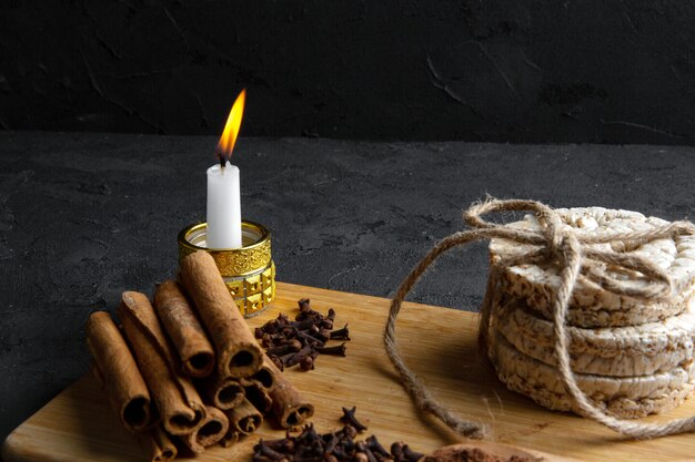 Vue latérale des pains de riz attachés avec une corde et un bâton de cannelle avec une bougie allumée sur planche de bois sur fond noir