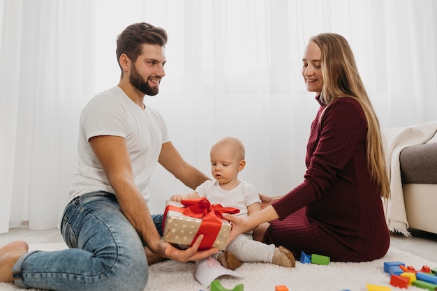 Vue latérale des parents à la maison avec leur bébé et cadeau