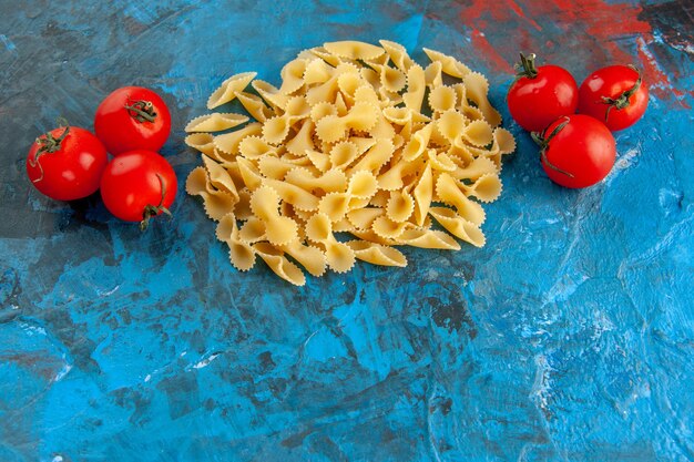 Vue latérale des pâtes farfalle crues et des tomates avec tige sur fond bleu