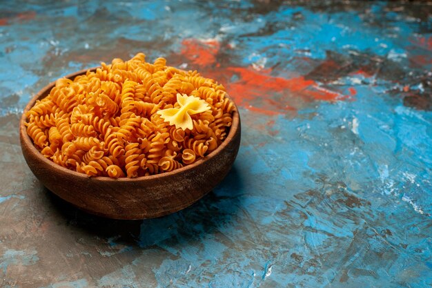 Vue latérale des pâtes italiennes crues dans un bol en bois marron sur une table bleue