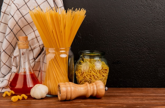 Vue latérale des pâtes spaghetti dans des bocaux avec du sel à l'ail beurre fondu et un tissu à carreaux sur une surface en bois et un fond noir avec copie espace