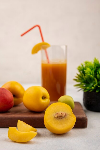 Vue latérale des pêches jaunes sucrées fraîches sur une planche de cuisine en bois avec du jus de pêche sur fond blanc