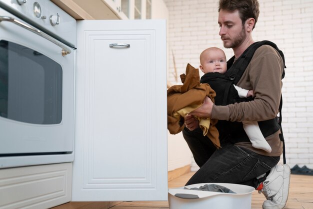 Photo gratuite vue latérale père faisant la lessive tout en portant bébé