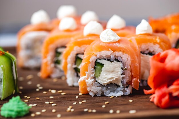 Vue latérale Philadelphia roll avec fromage à la crème concombre saumon wasabi gingembre et graines de sésame sur une planche