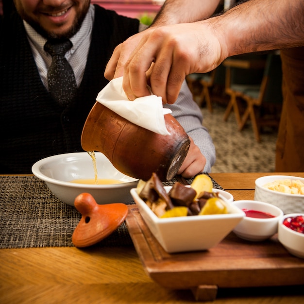 Vue latérale piti avec assiette profonde et vinaigre et humain dans une cruche d'argile sur table en bois