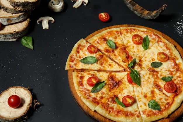 Vue latérale de la pizza sur un plateau avec des tomates et des champignons sur un tableau noir