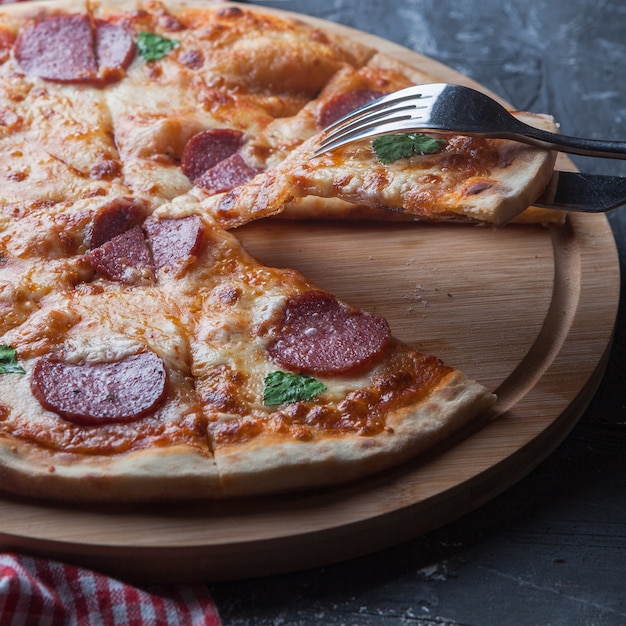 Vue latérale pizza à la saucisse avec serviette et fourchette en ustensiles de cuisine à bord