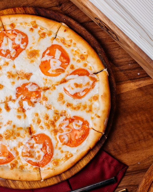 Vue latérale de la pizza à la tomate et au fromage sur une planche en bois ronde