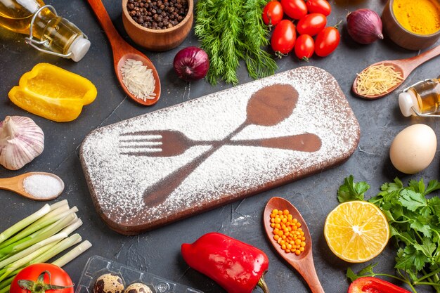 Vue latérale d'une planche à découper avec un couteau à fourche tiré par de la farine parmi des légumes frais différents paquets verts d'épices