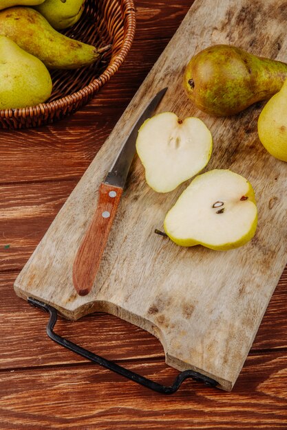 Vue latérale des poires mûres fraîches et des moitiés sur une planche à découper en bois avec couteau de cuisine sur fond rustique