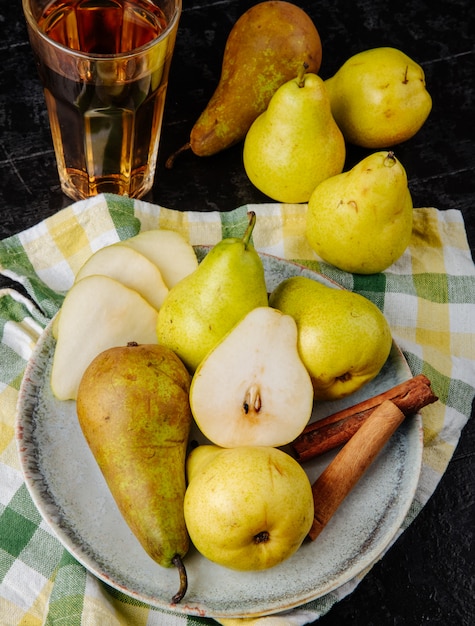 Photo gratuite vue latérale des poires vertes fraîches et des moitiés de poire dans une assiette et un verre de jus sur la table