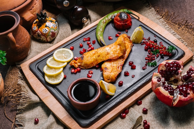 Vue latérale poisson grillé à la tomate et au piment grillé avec des tranches de citron à la grenade et de la sauce narsharab