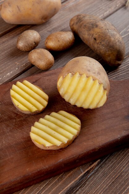 Vue latérale de la pomme de terre en tranches et coupées sur une surface en bois avec des pommes de terre entières sur fond de bois