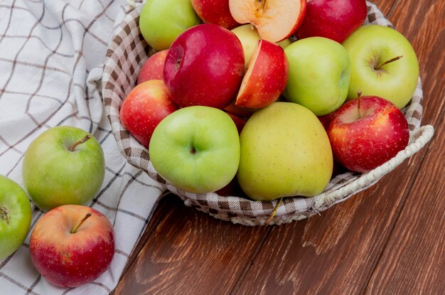 Vue latérale des pommes coupées et entières dans le panier et sur un tissu à carreaux sur une surface en bois