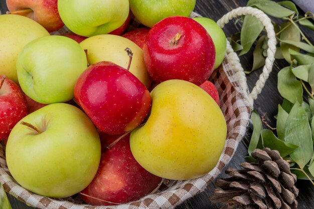 Vue latérale des pommes dans le panier avec pomme de pin et feuilles sur la surface en bois