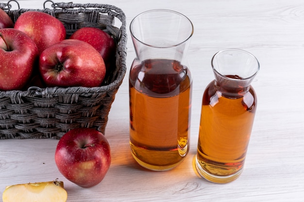 Vue latérale des pommes rouges dans le panier avec du jus sur une table en bois blanc