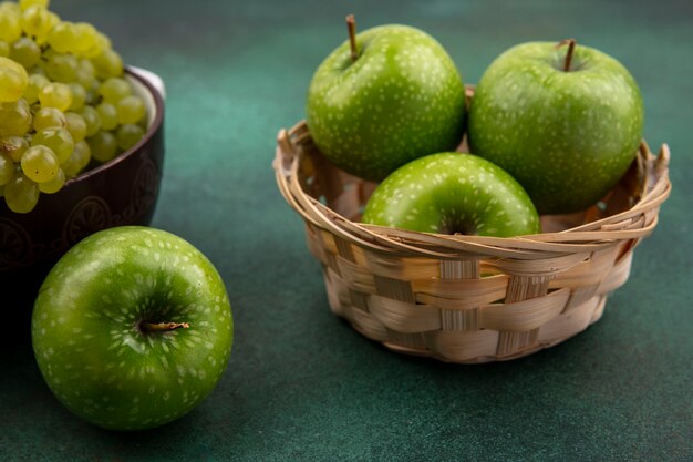 Vue latérale des pommes vertes dans un panier avec des raisins verts sur fond vert