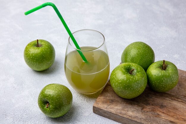 Vue latérale des pommes vertes avec du jus de pomme dans un verre et une paille verte sur fond blanc