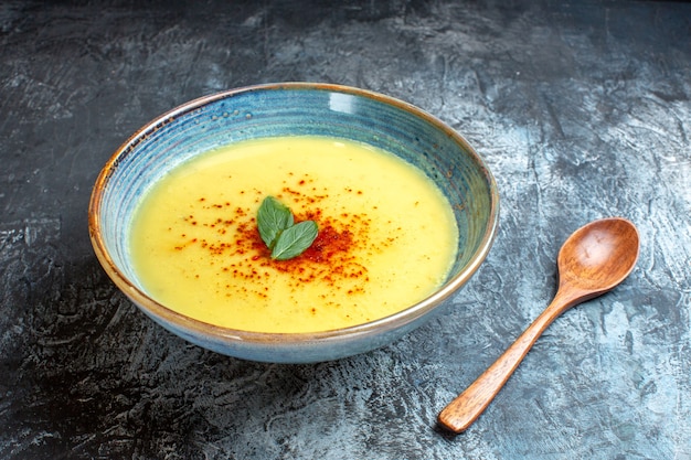 Vue latérale d'un pot bleu avec une soupe savoureuse servie avec de la menthe et une cuillère en bois sur une table bleue