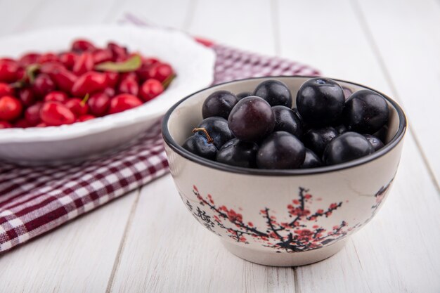 Vue latérale de la prune cerise dans un bol avec cornouiller sur une assiette