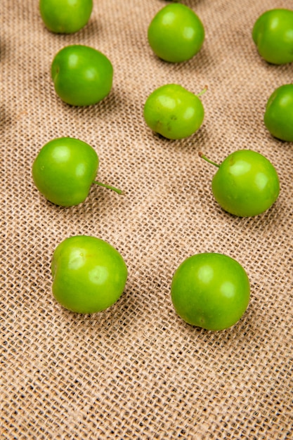 Vue latérale des prunes vertes aigres isolées sur la table d'un sac