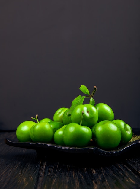 Vue Latérale De Prunes Vertes Aigres Avec De La Menthe Poivrée Séchée Sur Un Plateau Noir Sur Table Sombre