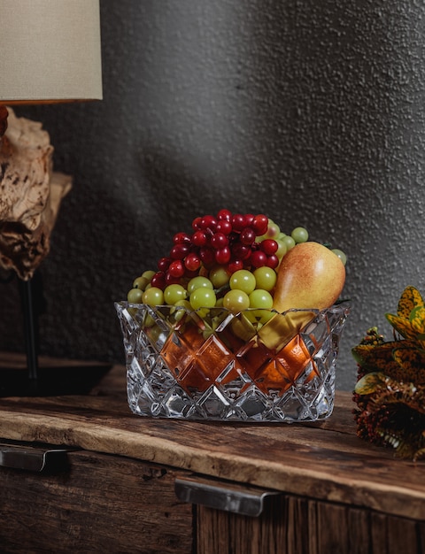 Photo gratuite vue latérale des raisins aux poires dans un vase en verre sur une armoire en bois sur mur sombre
