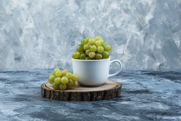 Vue latérale des raisins verts dans une tasse blanche sur fond de pièce de bois et de plâtre grungy. horizontal