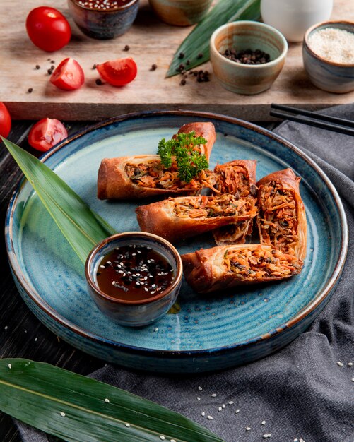 Vue latérale des rouleaux de printemps frits avec du poulet et des légumes servis avec de la sauce soja sur une assiette sur fond noir