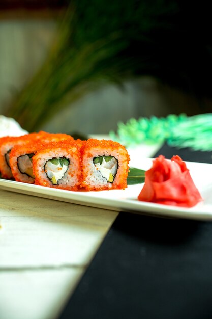 Vue latérale de rouleaux de sushi avec du fromage à la crème de chair de crabe et de l'avocat dans du caviar de poisson volant avec de la sauce de soja à l'obscurité