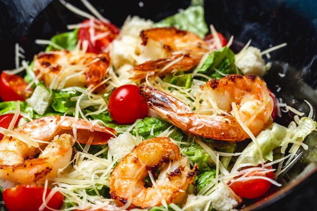 Vue latérale salade césar avec crevettes grillées laitue tomates cerises et parmesan sur une plaque