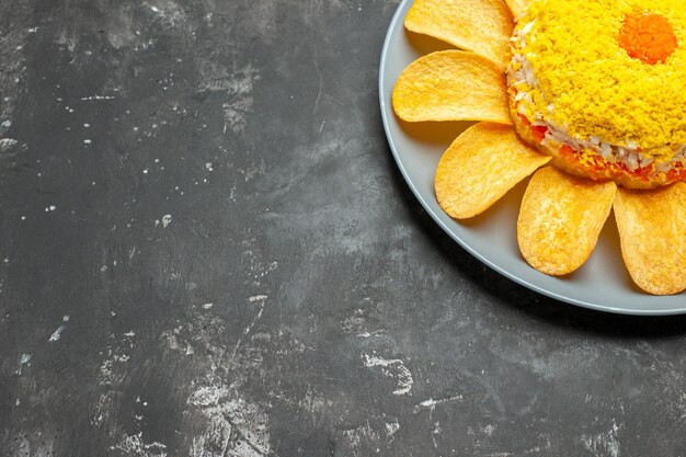 Vue latérale de la salade avec des frites autour sur une assiette sur fond gris foncé