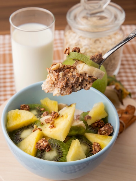 Vue latérale salade de fruits dans une assiette ananas kiwi avec granola sur une cuillère avec un verre de lait