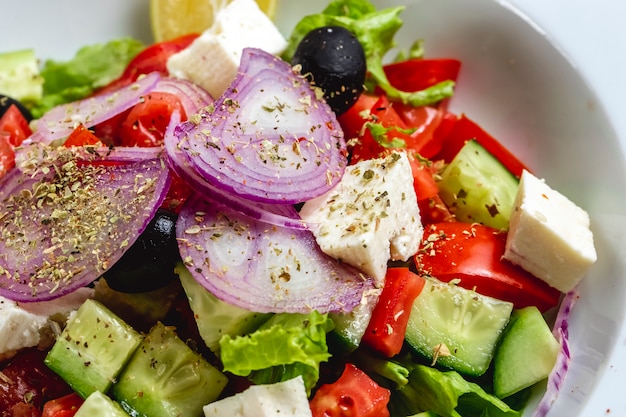 Vue latérale salade grecque au fromage blanc oignon rouge olive noire tomate concombre laitue origan et huile d'olive