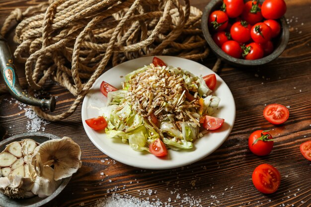 Vue latérale salade de légumes sur une assiette avec des tomates cerises dans un bol avec une corde sur la table