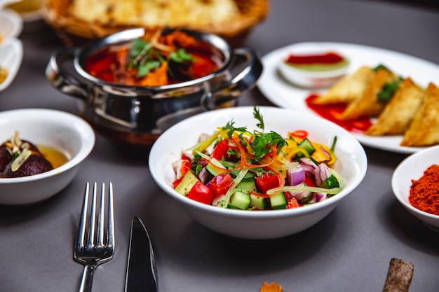 Vue latérale salade de légumes avec concombre oignon rouge poivron vert et poivre noir sur une plaque