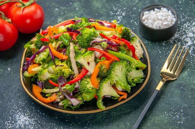 Vue latérale d'une salade végétalienne dans une assiette avec divers légumes et tomates à la fourchette avec tige sur fond sombre