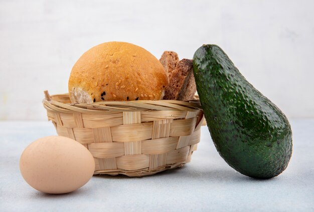 Vue latérale d'un seau de pains avec avocat et oeuf sur une surface blanche