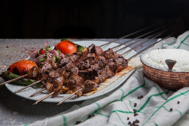 Vue latérale shish kebab sur des brochettes avec tomate et oignon et ayran en plaque blanche