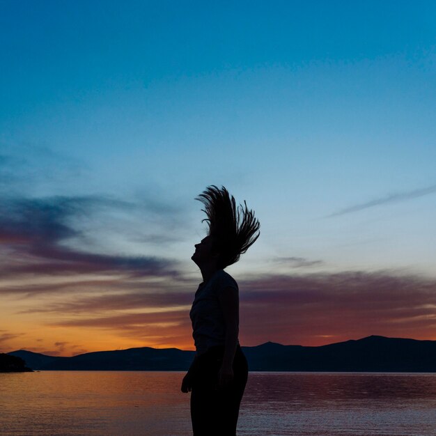 Vue latérale de la silhouette de la femme sur la plage au coucher du soleil