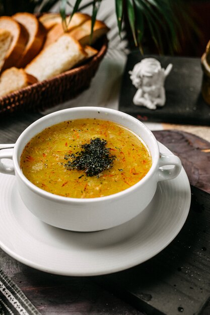 Vue latérale de la soupe de pois et lentilles au safran et aux herbes dans un bol blanc