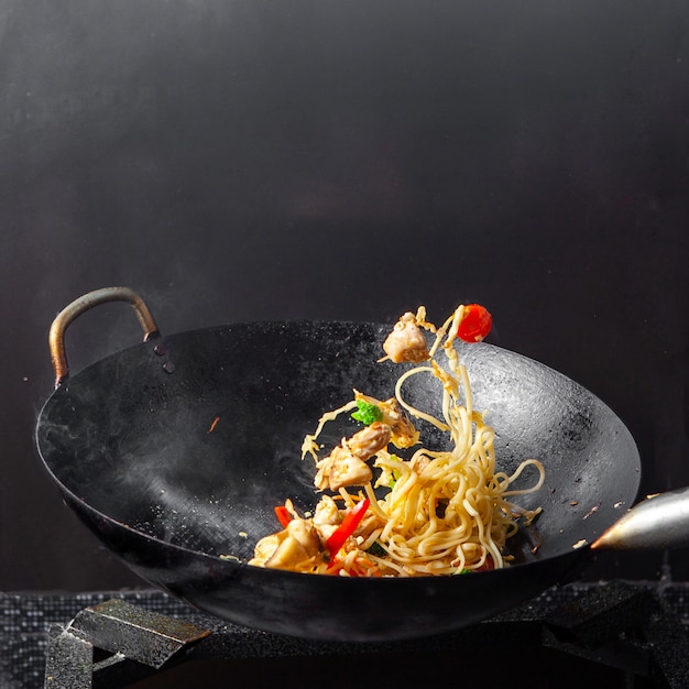 Vue latérale spaghetti dans une poêle sur fond noir.