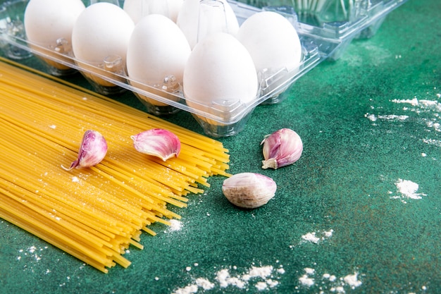 Vue latérale des spaghettis crus d'ail et d'œufs sur une surface verte