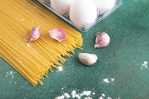 Vue latérale des spaghettis crus avec de l'ail et des œufs sur une surface verte