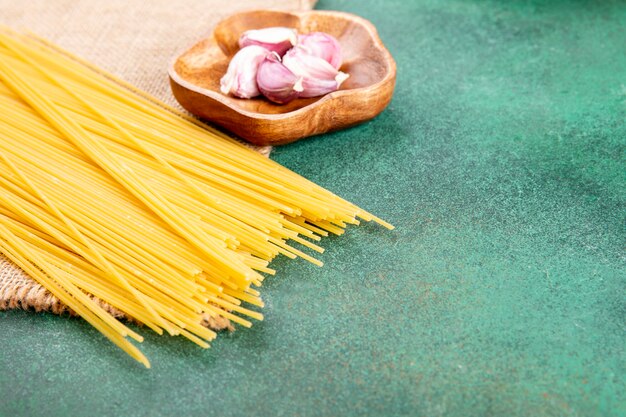 Vue latérale des spaghettis crus à l'ail sur une surface verte