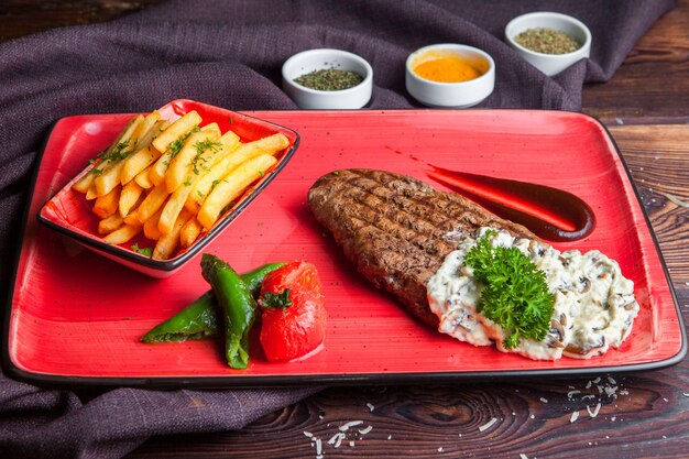 Vue latérale steak steak avec sauce aux pommes de terre frites, épices sur une plaque rouge