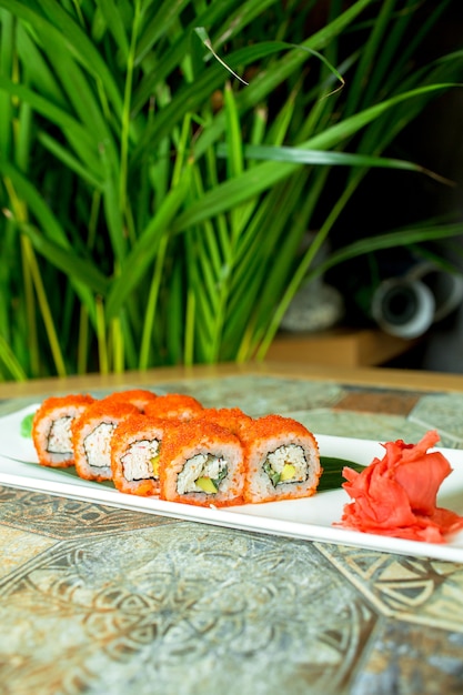 Vue latérale de sushi set rouleaux avec du fromage à la crème de chair de crabe et de l'avocat dans du caviar de poisson volant servi avec des tranches de gingembre sur vert